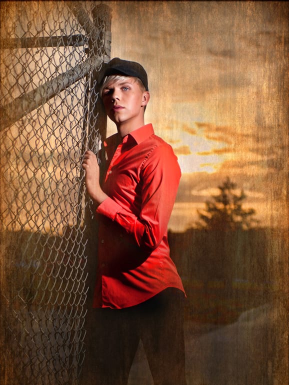 young man leaning against chain link fence at sunset