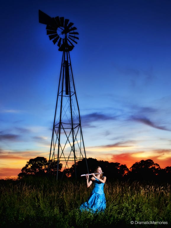 a musician playing her flute near an old windmill at sunset